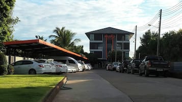 Hotel con zona de estacionamiento techada, varios coches aparcados y un edificio con un cartel.