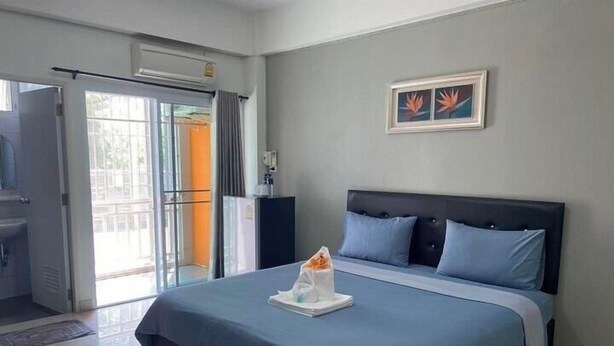 A hotel room with a bed, a small table with a tissue box, a picture on the wall, and a view through the door. - Tonsom Residence (Uttaradit)