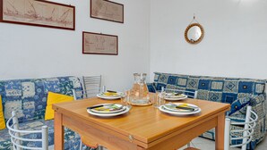 Ein Essbereich mit einem Holztisch, gedeckt für vier Personen, einer gemusterten Couch und gerahmten Bildern an der Wand.