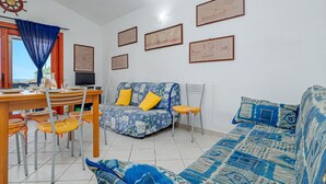 Ein Wohnzimmer mit Sofa, einem Esstisch mit Stühlen, einem Fernseher und gerahmten Kunstwerken an der Wand.
