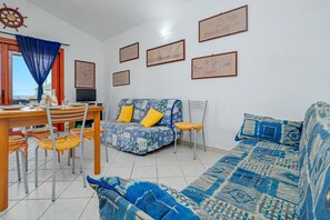 Un salon comprenant un canapé, une table à manger avec des chaises, un téléviseur et des œuvres d’art encadrées accrochées au mur.