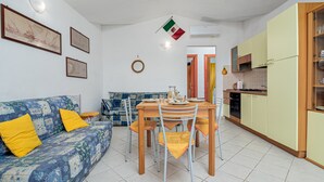 Ein Wohnzimmer mit Sofa, Esstisch, Stühlen und einer Küche mit Schränken und Geräten.