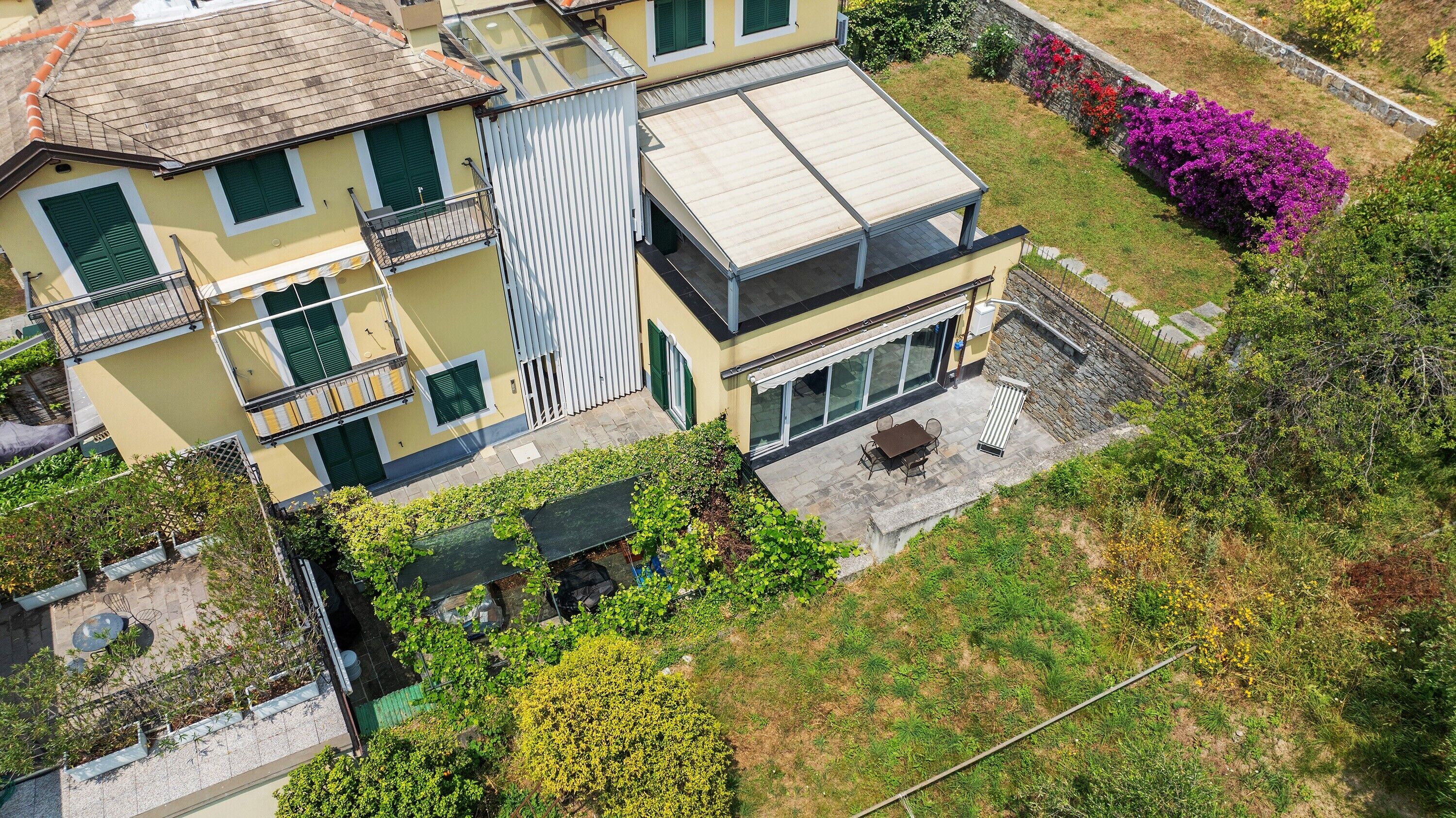 Ein mehrgeschossiges Wohngebäude mit flachem Dach, einem Balkon und einer Terrasse mit Gartenmöbeln.