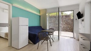 A compact room with a bed, a sofa, a dining table with chairs, a refrigerator, and a TV mounted on the wall. - Apartment 'Green House' with Private Terrace, Wi-Fi and Air Conditioning (Sestri Levante)