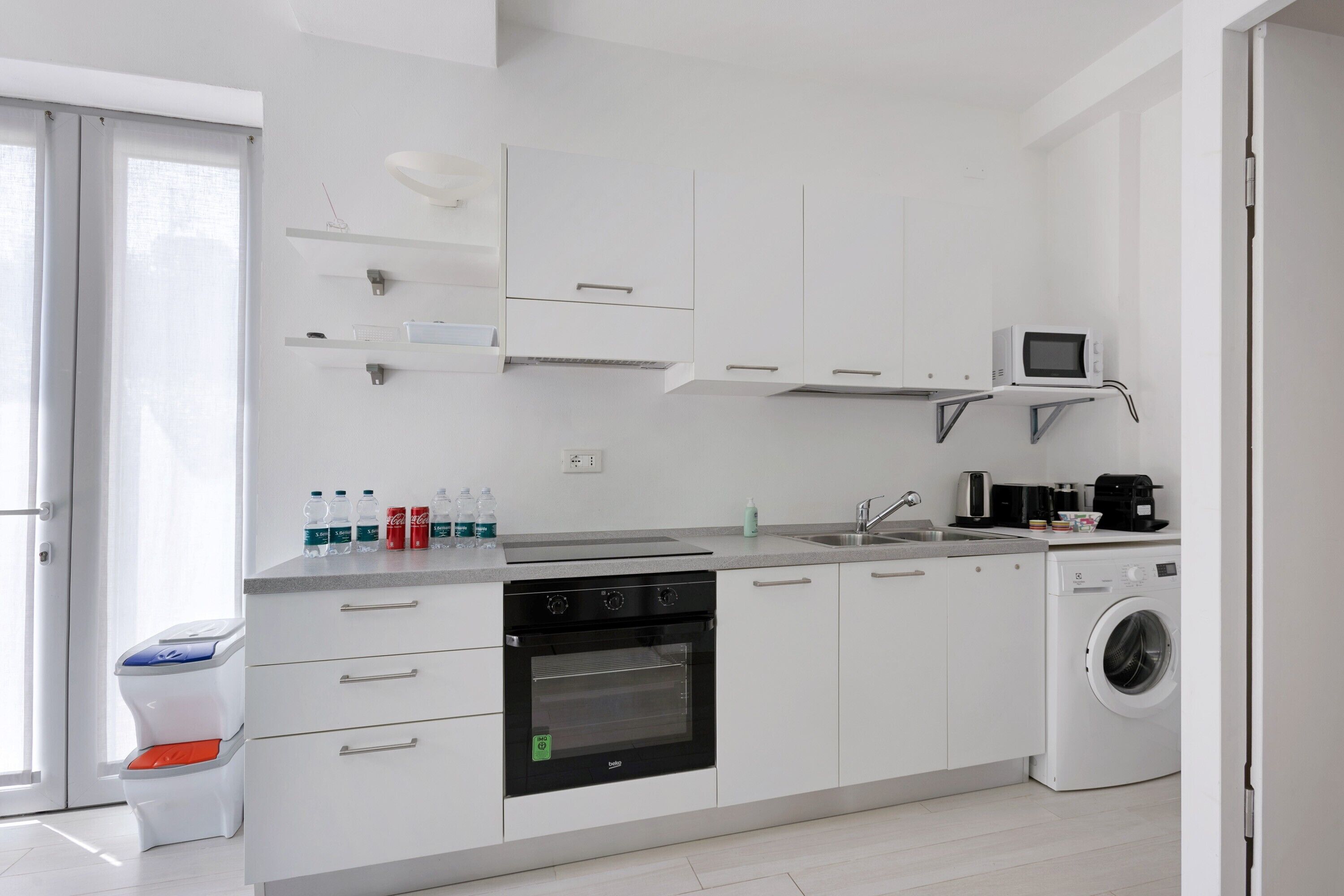 Una cocina moderna con armarios blancos, horno empotrado, microondas, lavadora y un lavaplatos.