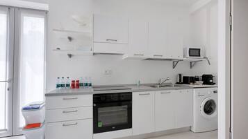 Una cocina moderna con armarios blancos, horno empotrado, microondas, lavadora y un lavaplatos.