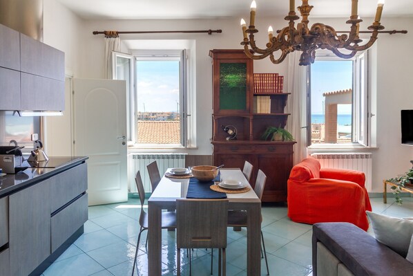 A modern kitchen with a dining area, a red sofa, and a view of the sea.
