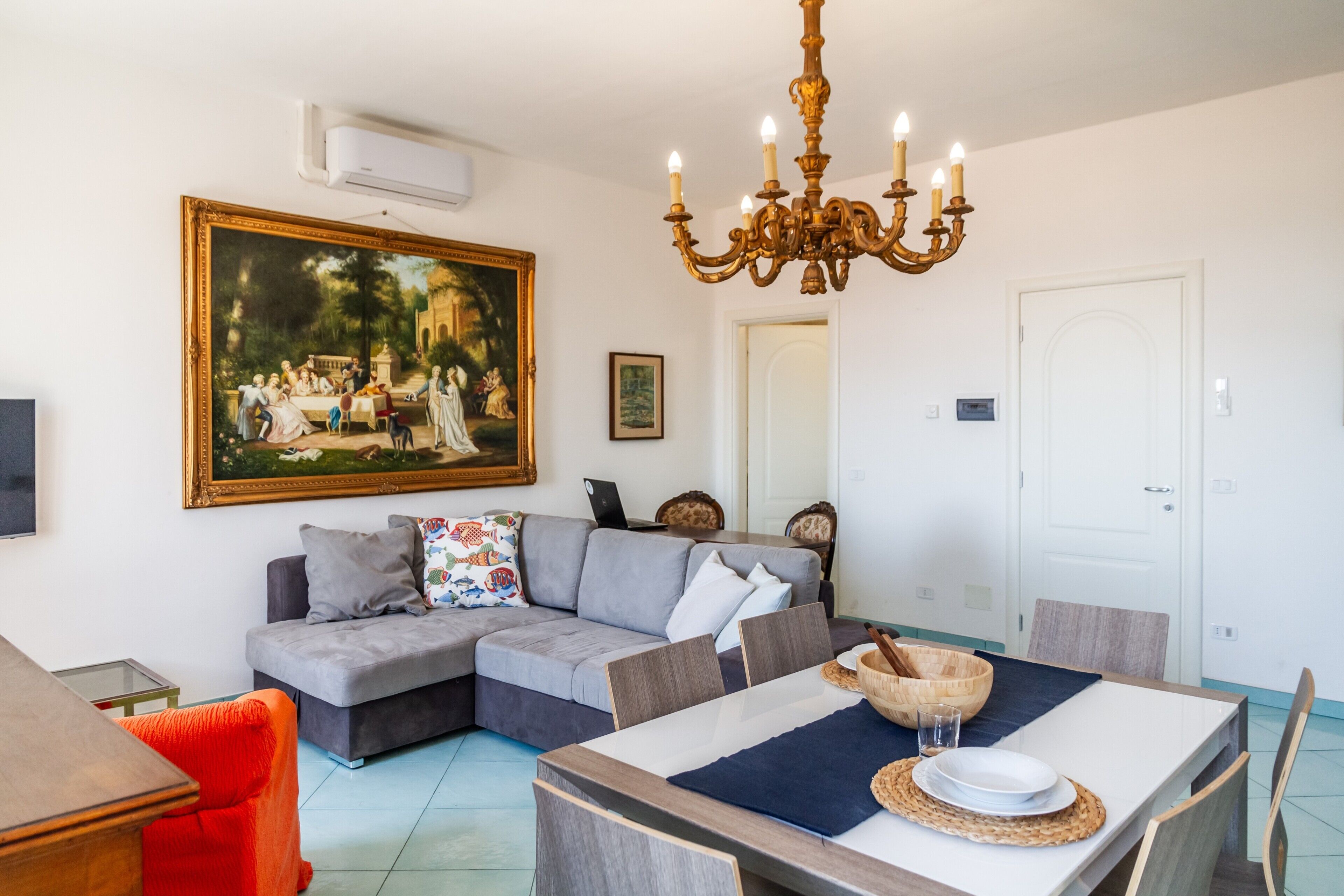 A living room with a sectional sofa, a dining table, and a chandelier.