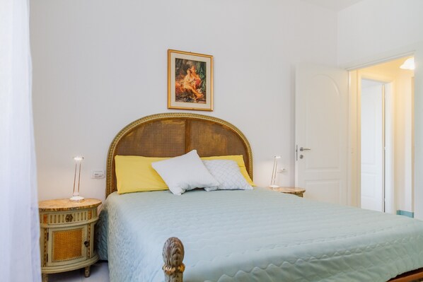 Un dormitorio con cama, mesita de noche, lámpara, una puerta y un cuadro en la pared.