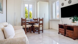 Ein Zimmer mit einer Couch, einem Esstisch mit Stühlen, einem Fernseher und einem Schrank.