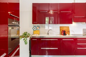 A modern kitchen with red cabinets, a stainless steel oven, and a wooden cutting board on the counter.