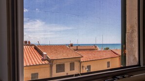 Blick aus dem Fenster auf Gebäude mit Terrakotta-Dächern, einen klaren Himmel und ein entferntes Gewässer.