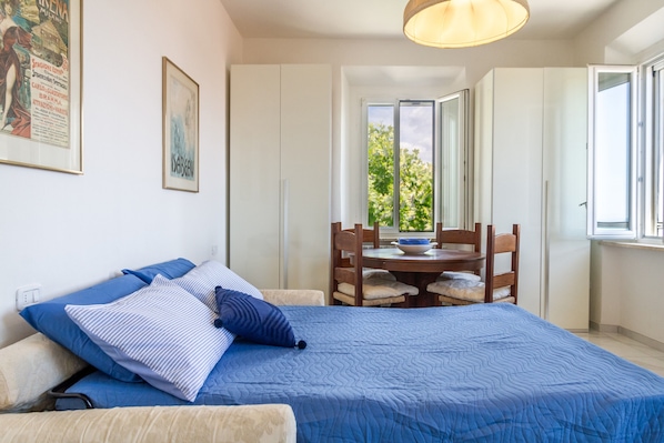 A bedroom with a bed, a dining table with chairs, a window, and a door.