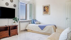 Ein Schlafzimmer mit einem Bett, einem Fernseher, einem Fenster, einer Heizung und einer Pflanze.