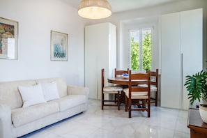A living room with a sofa, dining table, chairs, and a potted plant.