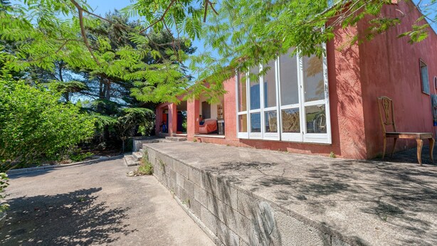 Un edificio rojo con ventanas amplias, un sendero de piedra y abundante vegetación.