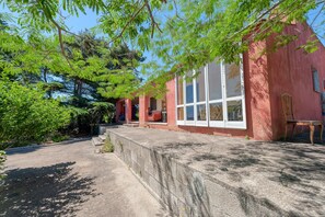 A red building with large windows, a stone pathway, and surrounding greenery.