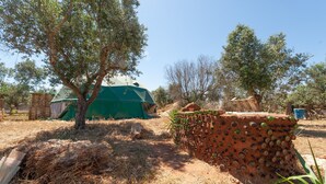 Entorno rústico al aire libre con una tienda verde, una estructura de ladrillo con hendiduras circulares y vegetación escasa.