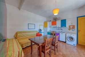 Un espace de vie compact comprenant un canapé, une table à manger, des chaises, un lave-linge et un coin cuisine.