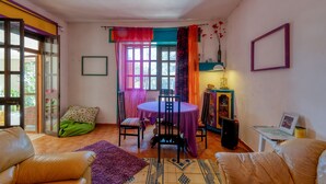 A room with a dining table, chairs, a sofa, a small table with a lamp, and a picture frame on the wall.