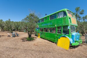 A green double-decker bus parked in a dry, grassy area with trees and a clear blue sky. - Holiday Home 'Sprocketlandia' with Private Terrace, Shared Garden and Wi-Fi (Frigole)