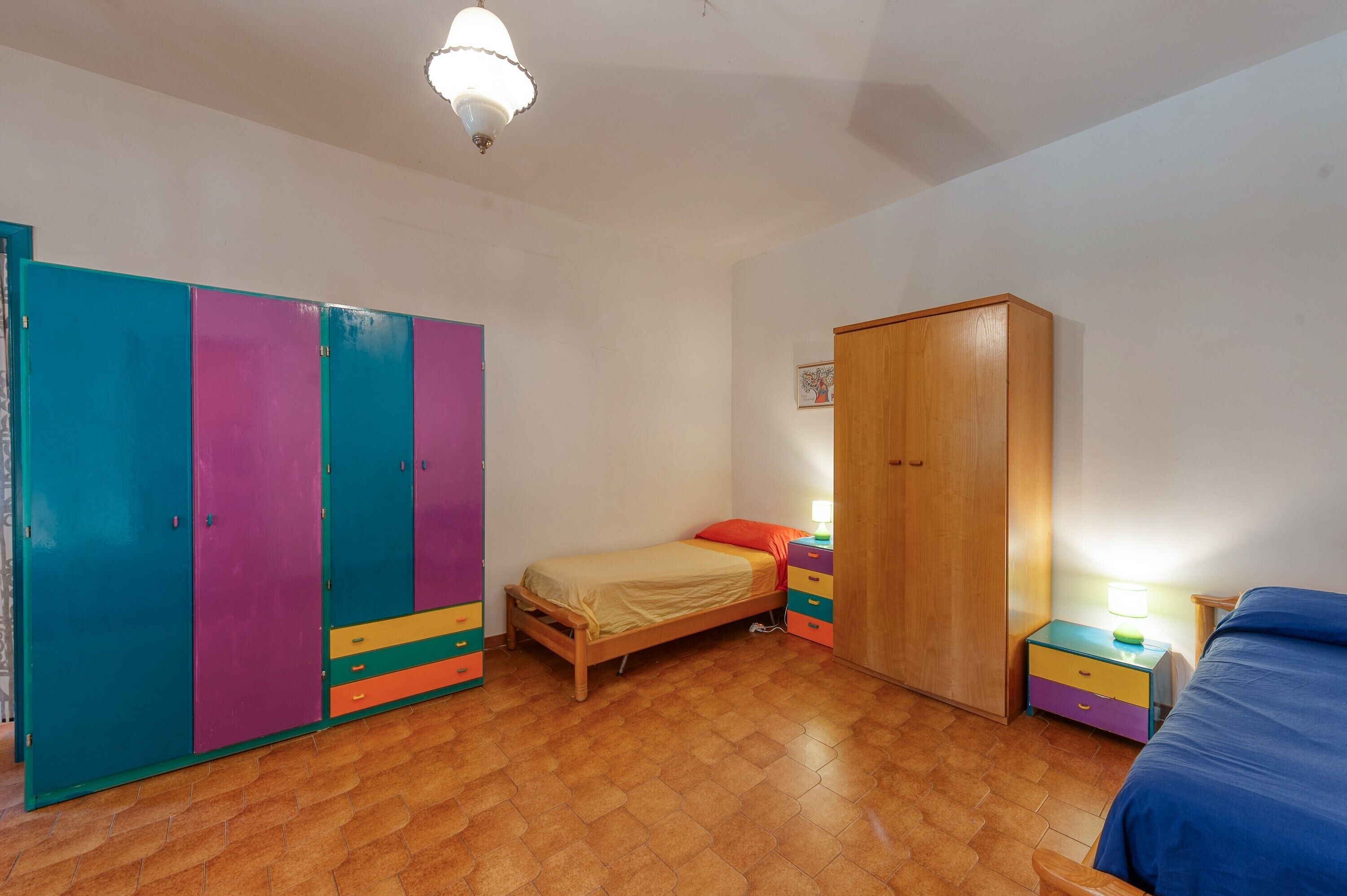 Une chambre à coucher avec un lit, une armoire, une table de chevet et une lampe.
