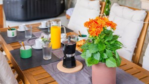 Ein Holztisch mit einer rosa Blumenvase, einer Kaffeemaschine und einem Glas Orangensaft.