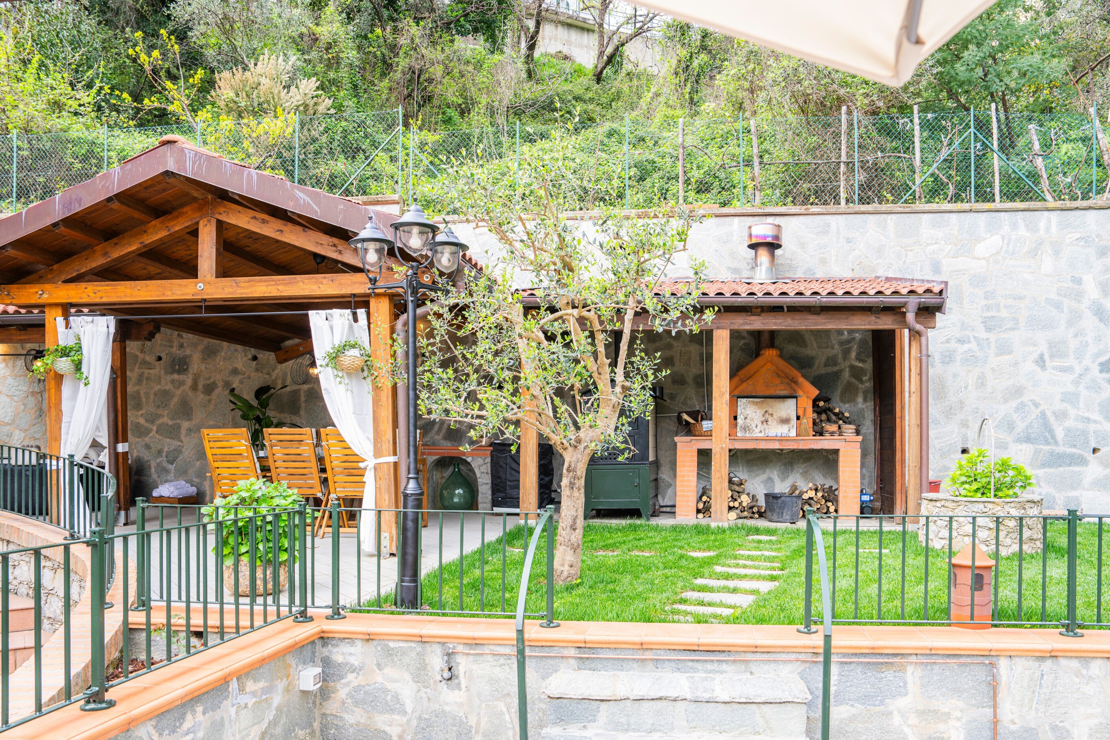 Ein Gebäude aus Stein mit einer Holzpergola, Sitzgelegenheiten im Freien und einem Gartenbereich.