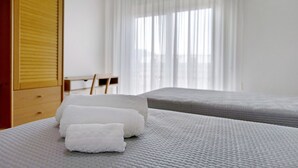 Une chambre d’hôtel avec un lit, une armoire en bois, un bureau et une fenêtre avec des rideaux légers.