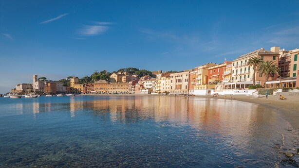 Une ville côtière avec des bâtiments le long du front de mer, une eau d’un bleu limpide et une plage paisible.