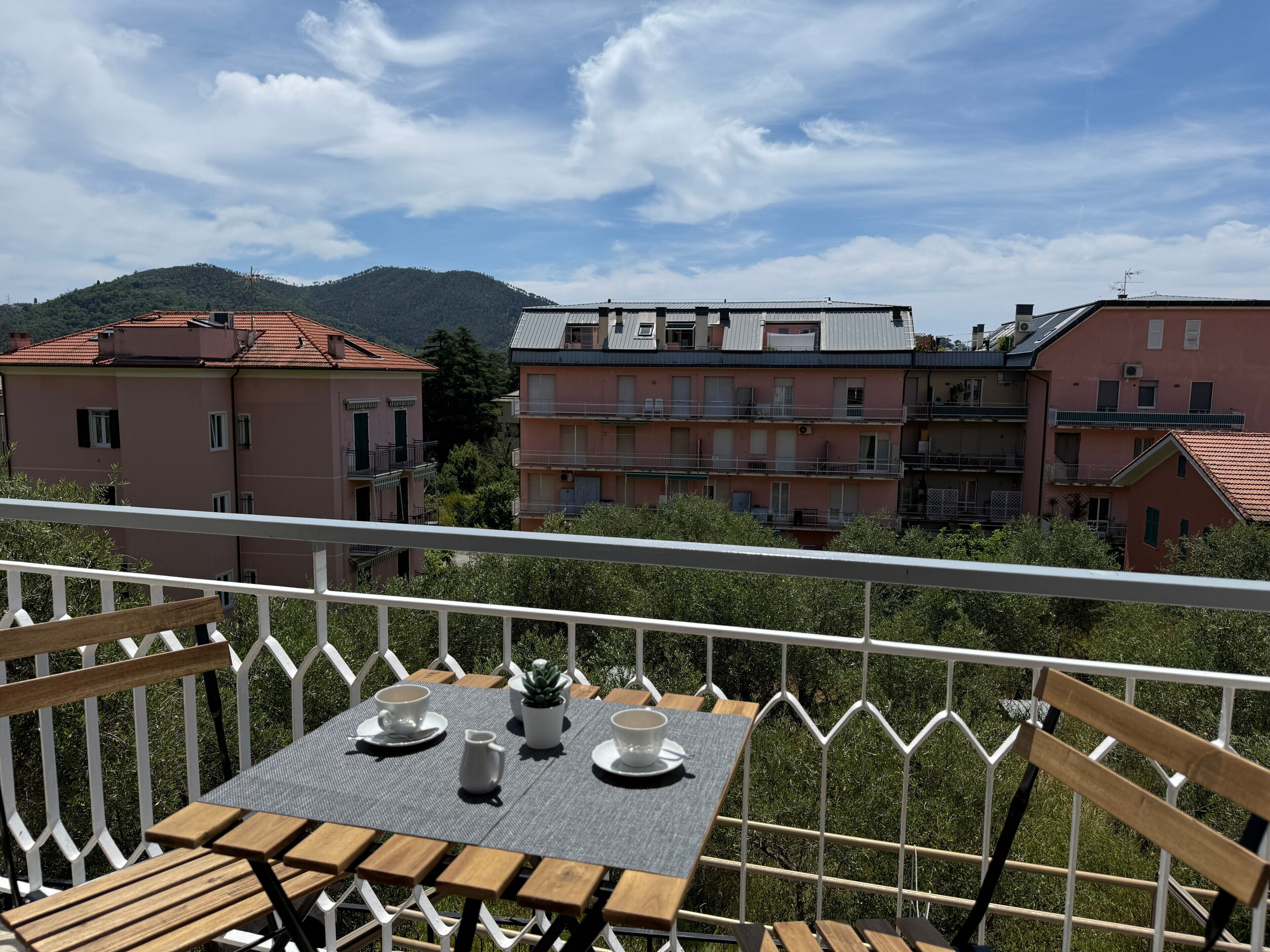 Ein Balkon mit Tisch für zwei Personen, Blick auf eine Häuserzeile und einen Berg.