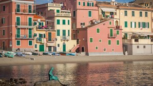 Une ville côtière aux bâtiments aux couleurs vives, avec une statue sur la plage et des bateaux amarrés à proximité.