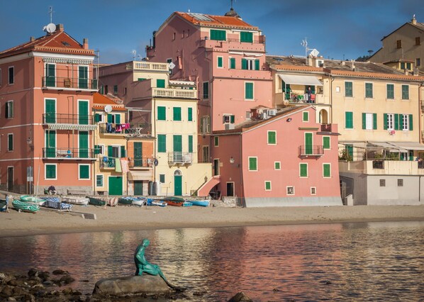 A coastal town with colorful buildings, a statue on the shore, and boats docked nearby.
