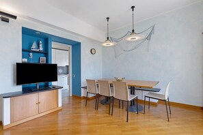 A dining area with a wooden table, six chairs, a flat-screen TV on a cabinet, and a wall with a nautical-themed mural.