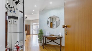 Un couloir avec un plancher en bois, un miroir rond accroché au mur, un bureau avec des papiers, une plante en pot et un extincteur.