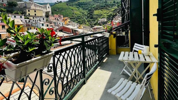 A balcony with a view of a hillside town, a table with chairs, and potted plants.