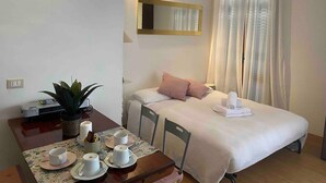 A bedroom with a bed, a bedside table with cups and a plant, a ceiling fan, and a window with curtains.