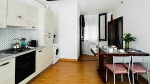 A compact kitchen with a washing machine, a dining area with a table and chairs, and a bed in the foreground.