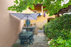 An outdoor patio with a table and chairs, a large umbrella, and potted plants.
