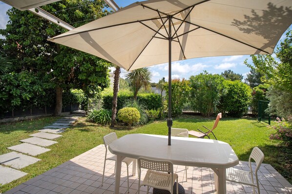 A patio with a table and chairs, surrounded by a garden with a variety of plants and a stone pathway.