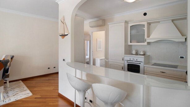 A modern kitchen with white cabinetry, a built-in oven, and a glass island with bar stools. - Apartment 'Avocado' with Shared Pool, Wi-Fi and Air Conditioning (Diano Castello)
