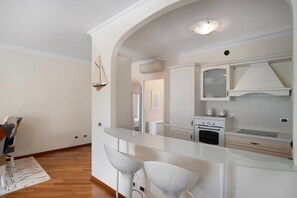A modern kitchen with white cabinetry, a built-in oven, and a glass island with bar stools.
