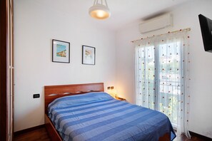 A bedroom with a bed, two framed pictures on the wall, a bedside lamp, and a window with curtains.