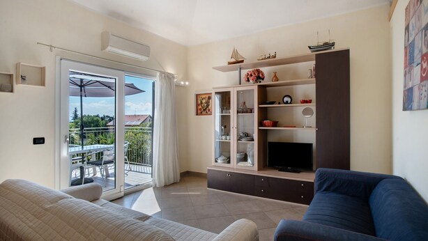 Una sala de estar con sofá, televisor, mueble y balcón con mesa y sombrilla.
