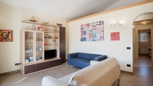 Una sala de estar con un sofá, televisión, aparador con cristalería y obras de arte en las paredes.