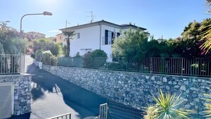 Una calle residencial con un muro de piedra, una reja metálica y un cielo azul despejado.