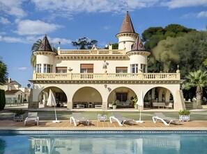 Un gran edificio parecido a un castillo con varias torres, una piscina y zonas de estar al aire libre.