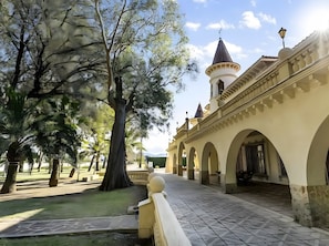Un patio con un sendero, árboles y un edificio con arcos y una torre.