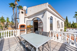 Un edificio blanco con techo de tejas, un balcón con barandilla blanca y una mesa con sillas.