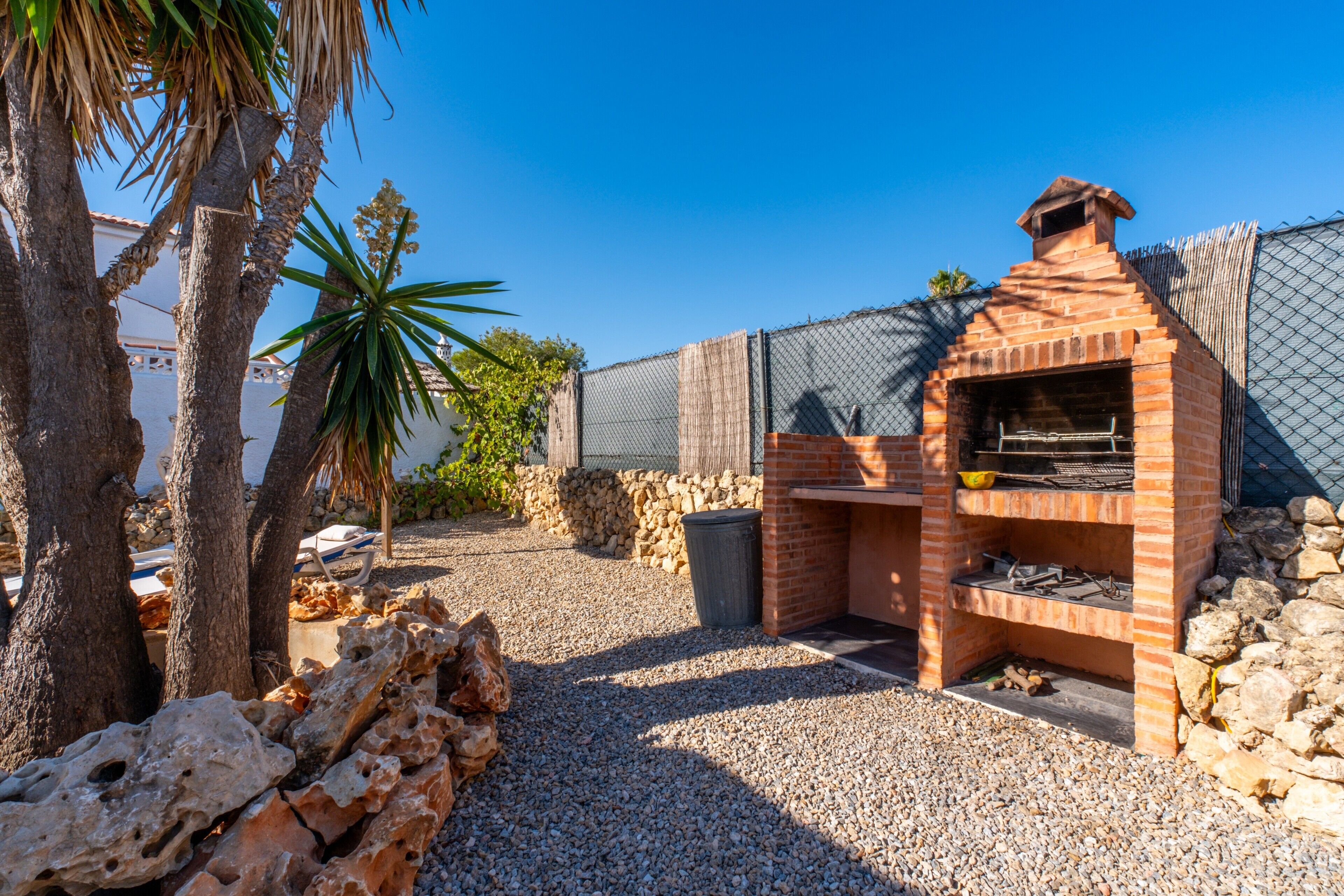 A brick outdoor grill area with a stone wall and palm trees.
